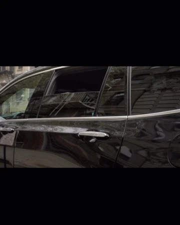 Side view of a shiny black SUV parked outdoors, reflecting the surroundings in its windows. The vehicle is parked on a street.