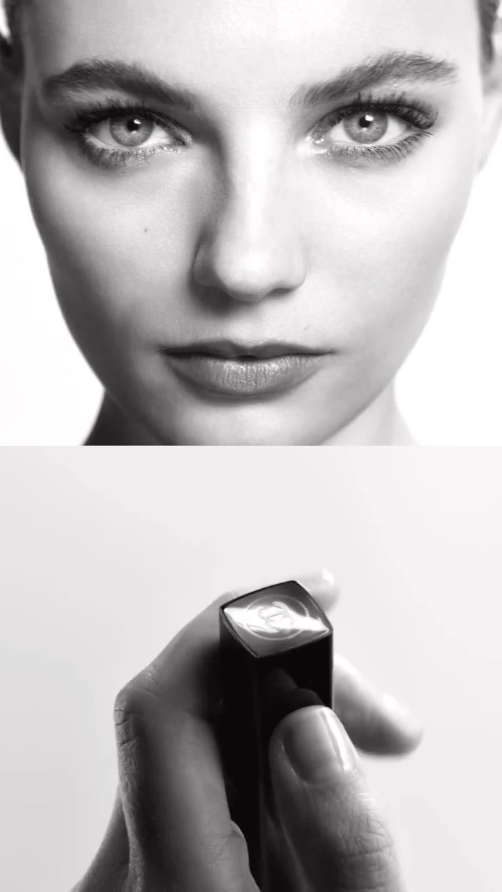 Close-up shot in black and white featuring a woman's face and a hand holding lipstick against a white background.