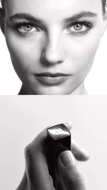 Close-up shot in black and white featuring a woman's face and a hand holding lipstick against a white background.