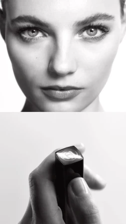 Close-up shot in black and white featuring a woman's face and a hand holding lipstick against a white background.