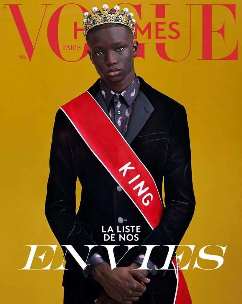 Vogue cover featuring a Black male model wearing a crown, velvet blazer, and a red sash with the word 'KING' on a yellow background.