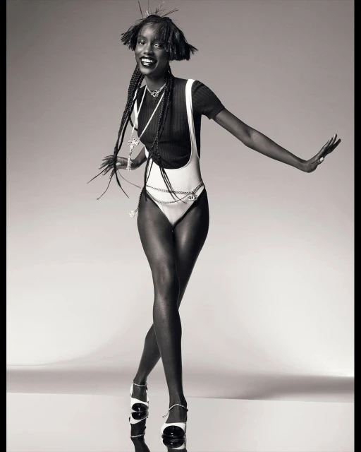 Monochrome studio shot of a slender African woman in a white bodysuit and black top, posing with outstretched arms and smiling.