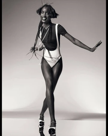 Monochrome studio shot of a slender African woman in a white bodysuit and black top, posing with outstretched arms and smiling.