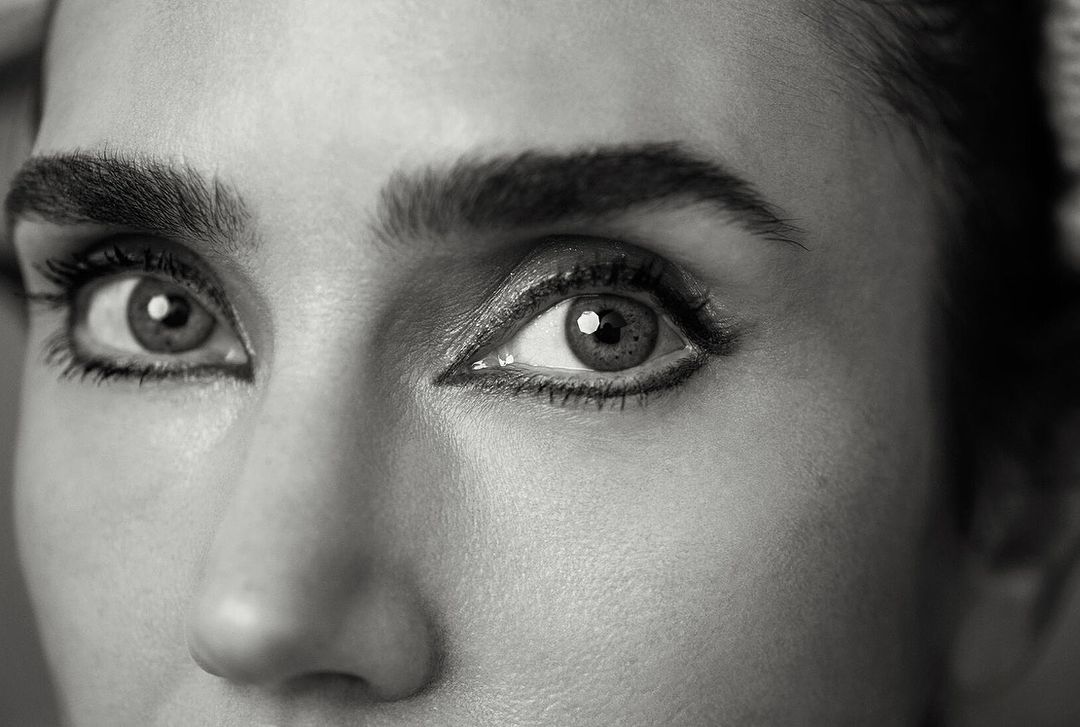 Close-up black and white portrait of a woman's face highlighting her eyes with eyeliner and defined eyebrows, captured with natural light.