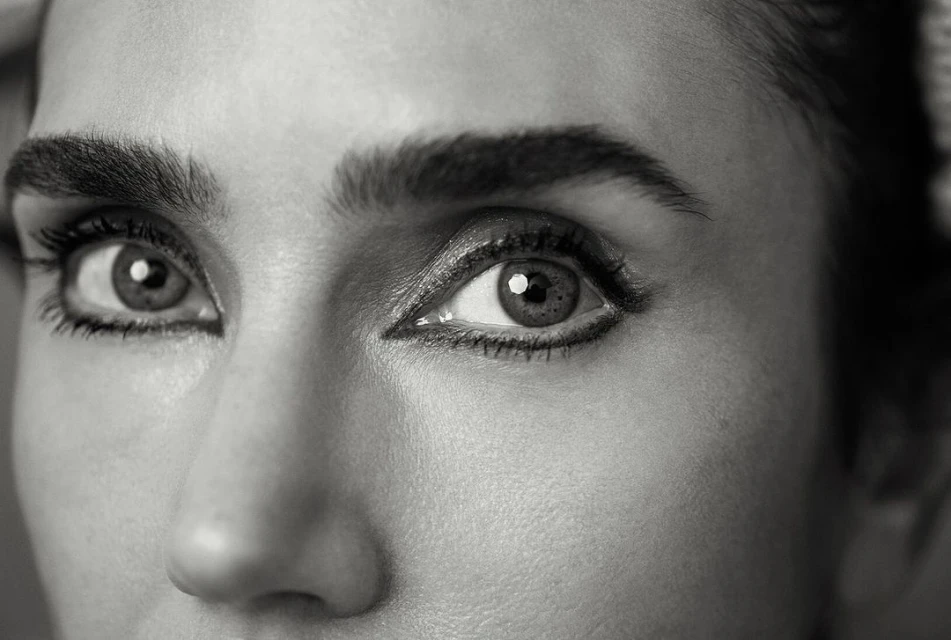 Close-up black and white portrait of a woman's face highlighting her eyes with eyeliner and defined eyebrows, captured with natural light.