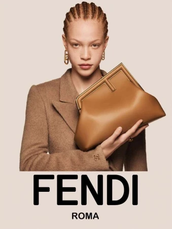 Model with braided hair wearing a camel blazer holding a tan leather clutch by Craig McDean