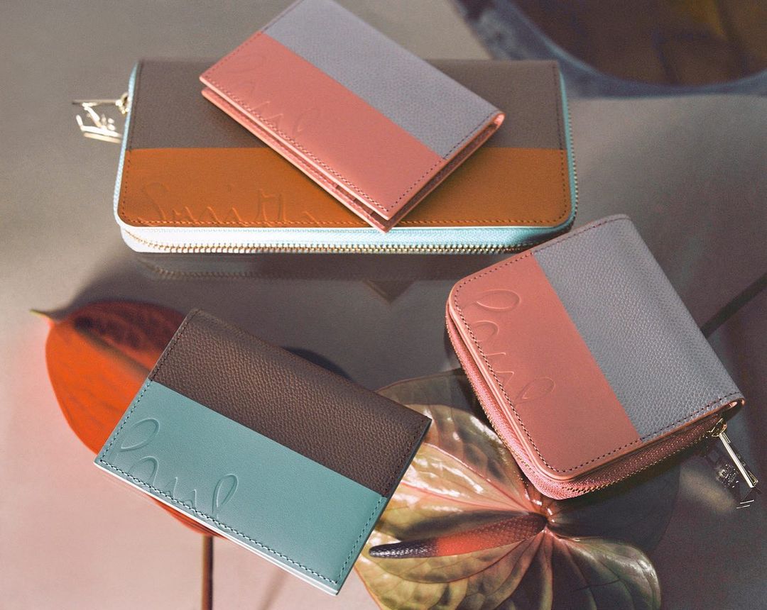 Arrangement of Paul Smith brand wallets and card holders in various colors on a reflective surface with Anthurium flowers.