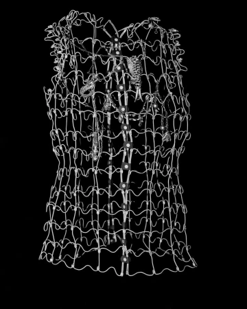 A wire mesh sculptural garment with hanging metallic charms displayed against a solid black background.