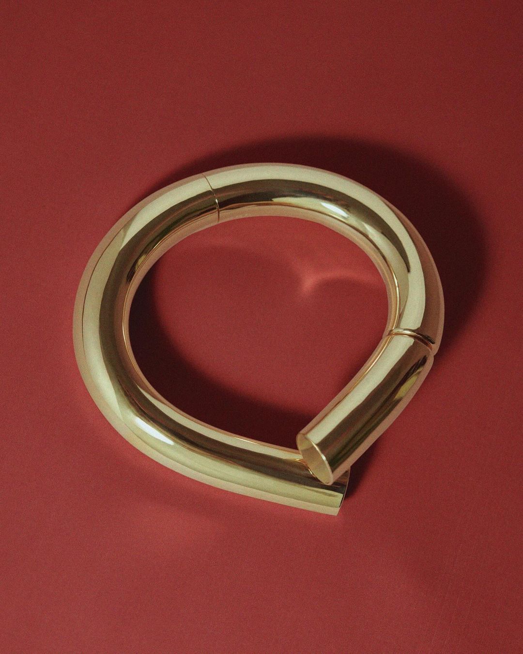 Close-up studio shot of a curved, seamless gold metal loop resting on a solid red surface, highlighting its smooth texture.
