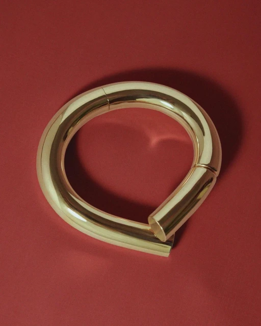 Close-up studio shot of a curved, seamless gold metal loop resting on a solid red surface, highlighting its smooth texture.