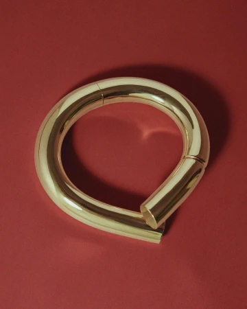 Close-up studio shot of a curved, seamless gold metal loop resting on a solid red surface, highlighting its smooth texture.