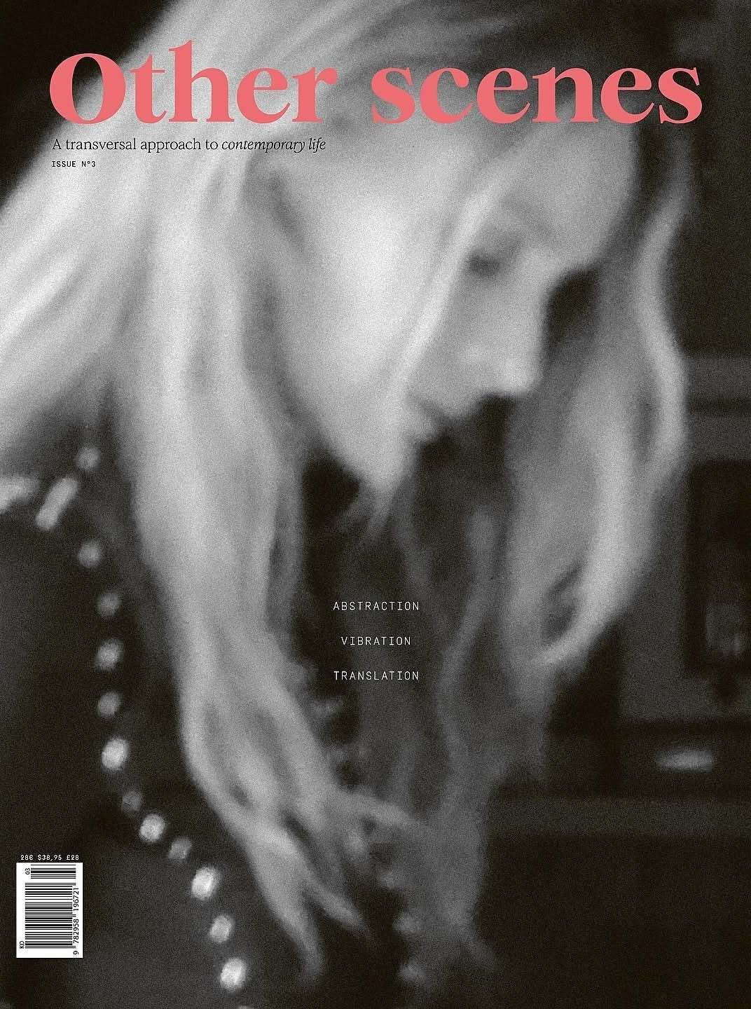 Magazine cover featuring a blurry portrait of a blonde woman in a black and white photo with pink text overlay.