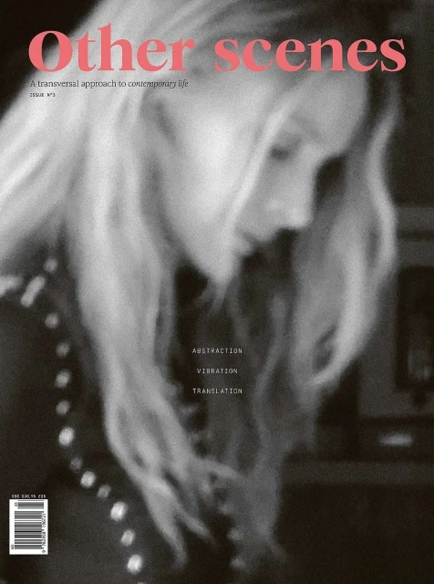 Magazine cover featuring a blurry portrait of a blonde woman in a black and white photo with pink text overlay.
