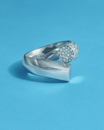 Close-up of a modern silver metal ring set with sparkling diamonds on a smooth blue surface in a jewelry or fashion context.