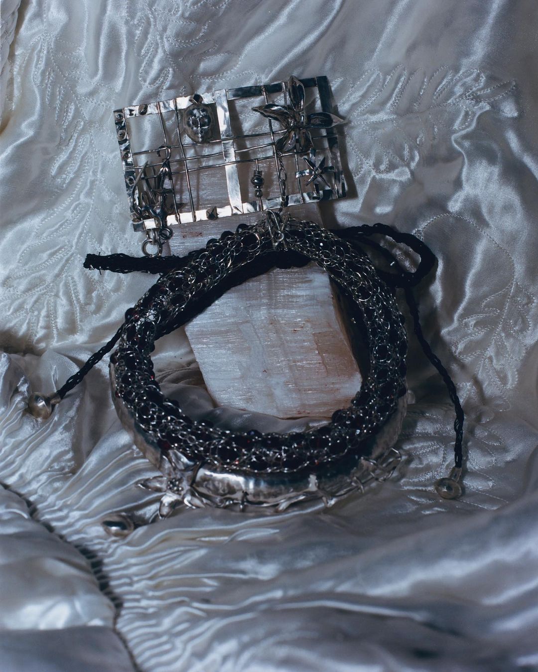 An arrangement of silver jewellery, including a necklace and brooch, displayed on a white satin fabric, showcasing metalwork and design details.