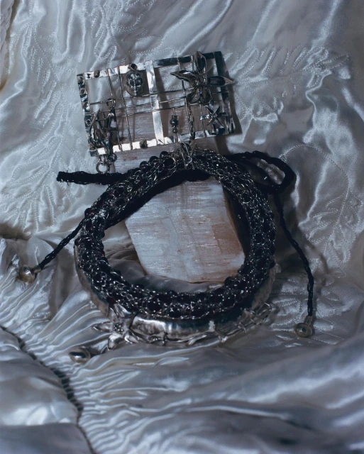 An arrangement of silver jewellery, including a necklace and brooch, displayed on a white satin fabric, showcasing metalwork and design details.