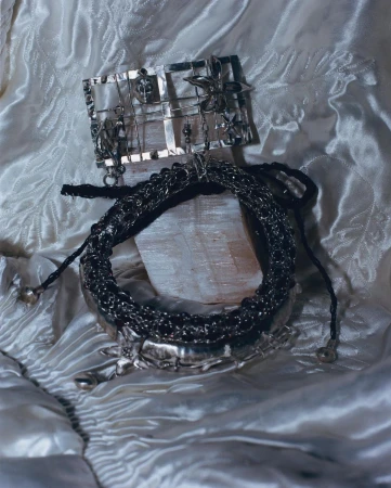 An arrangement of silver jewellery, including a necklace and brooch, displayed on a white satin fabric, showcasing metalwork and design details.