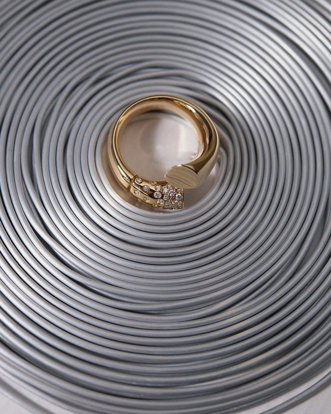 Close-up of a gold ring with diamond accents on a textured silver coiled metal background. Elegant jewelry shot for fashion or retail.