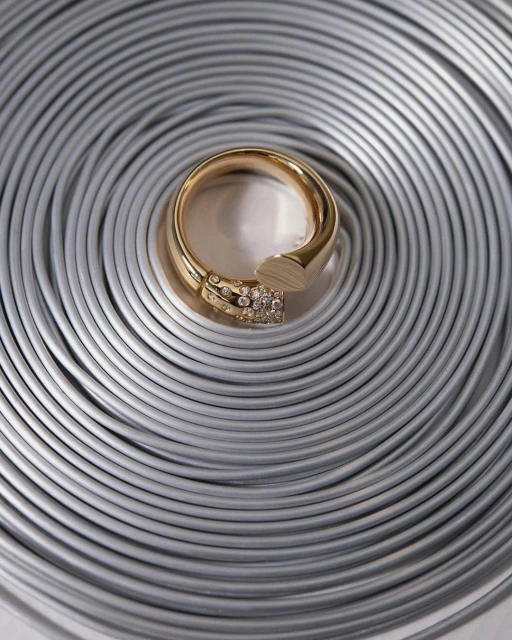 Close-up of a gold ring with diamond accents on a textured silver coiled metal background. Elegant jewelry shot for fashion or retail.