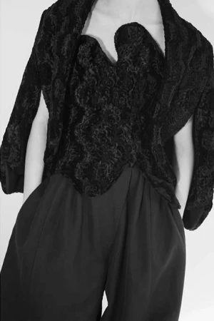 Model in textured black strapless top and matching capelet with dark trousers against a white background