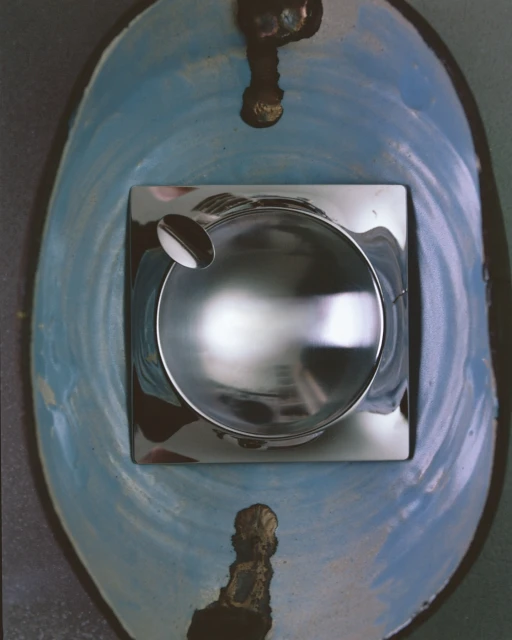 Close-up of a modern, silver ashtray centered on a blue-painted surface with decorative drips, offering a unique blend of functionality and art.