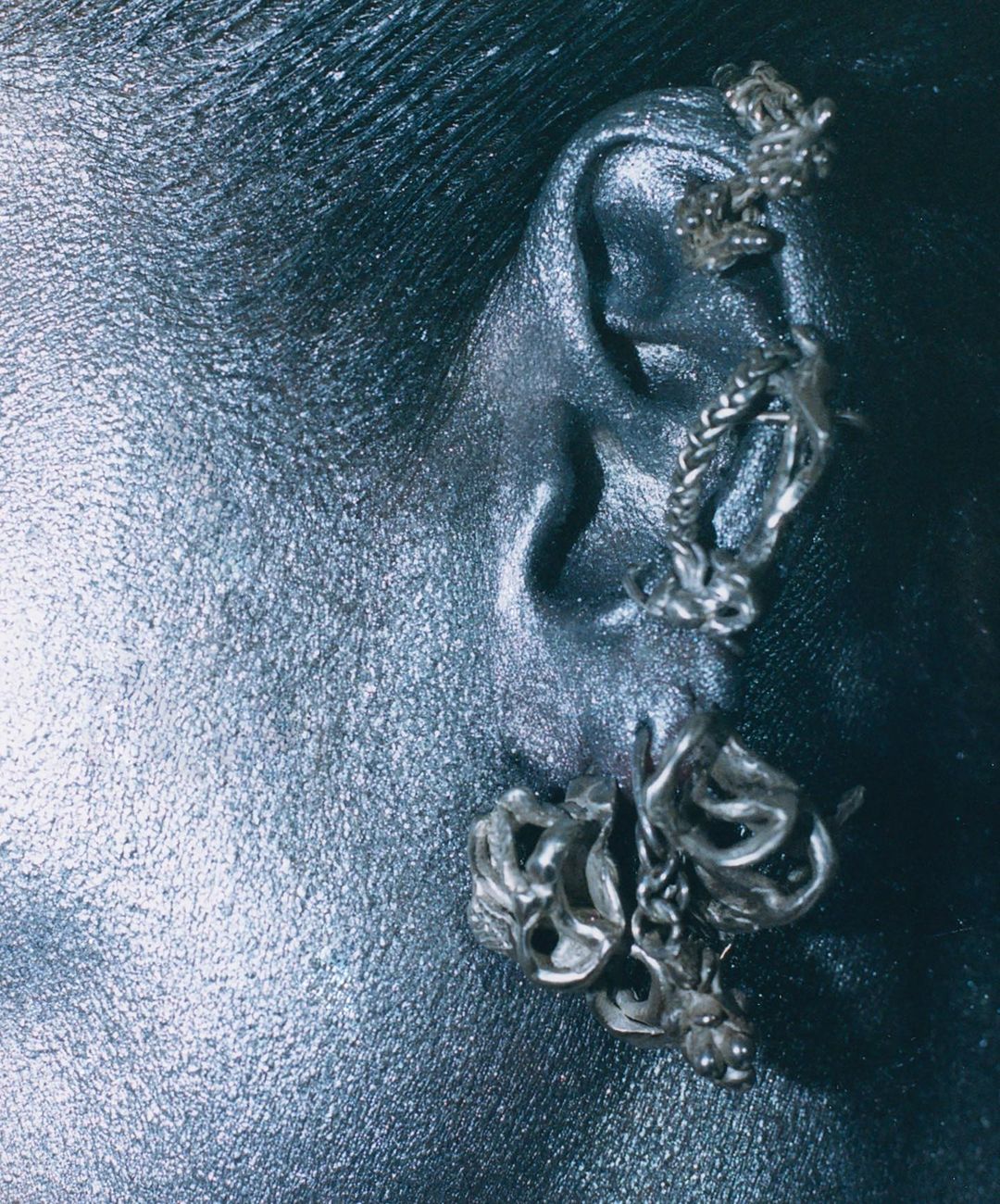 Close-up of a human ear with three textured silver ear cuffs or earrings, set against a dark background, accentuating the jewelry.