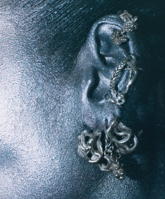 Close-up of a human ear with three textured silver ear cuffs or earrings, set against a dark background, accentuating the jewelry.