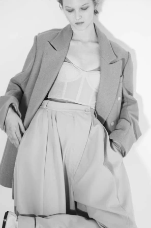 Model wearing an oversized tailored blazer over a light bustier and pleated high-waist trousers against a plain white studio background.