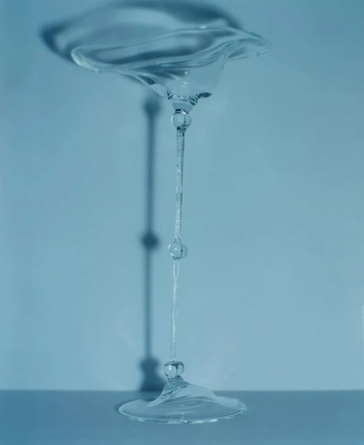 Conceptual studio photograph of an upside-down, clear glass goblet, with its shadow visible against a solid, light blue background.