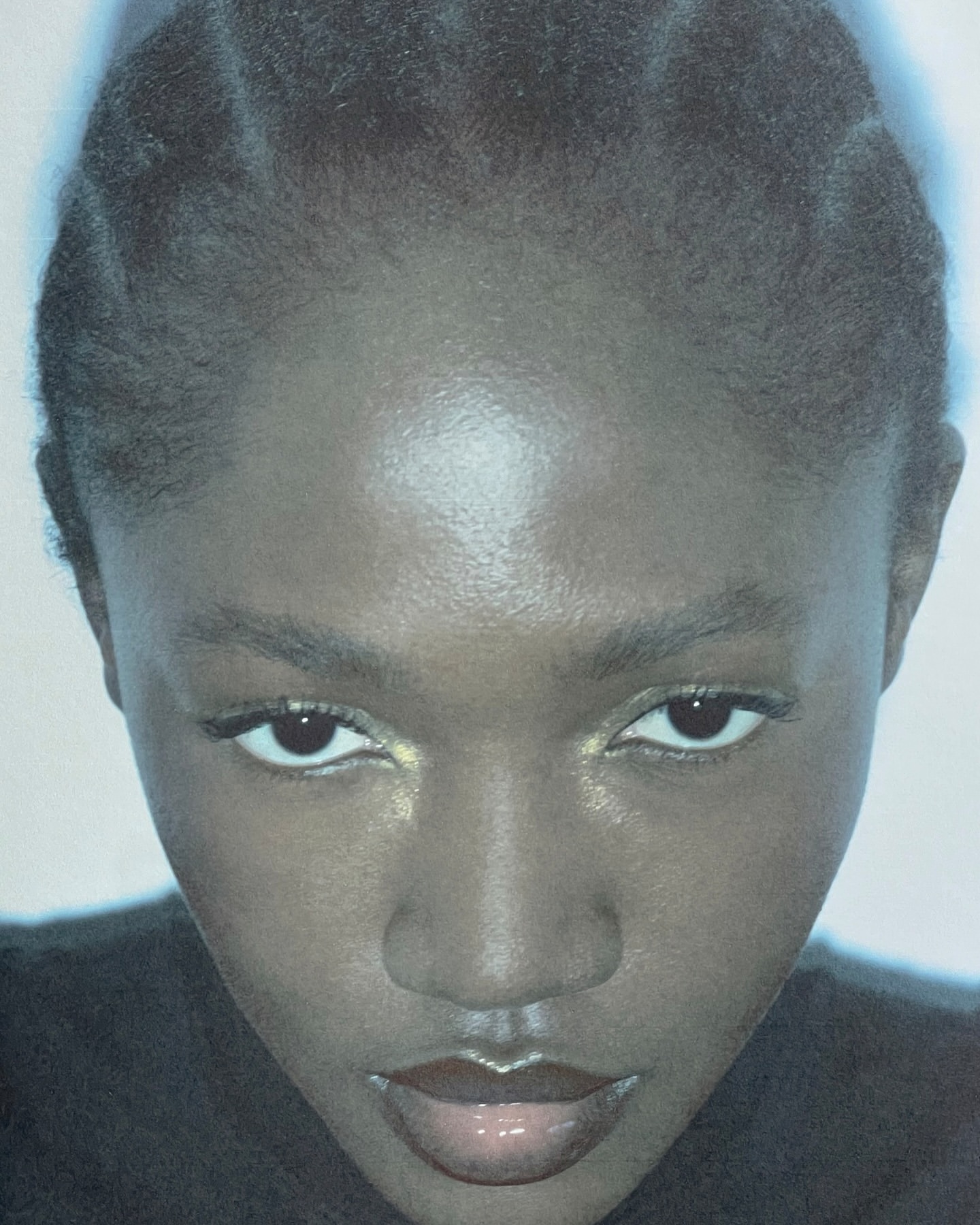 Close-up portrait of an adult female with dark skin, glossy lips, and braided hair, facing the camera with a neutral facial expression.