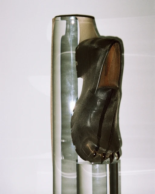 Studio still life of a shiny black leather shoe on a clear acrylic base with vertical acrylic rods against a white background.