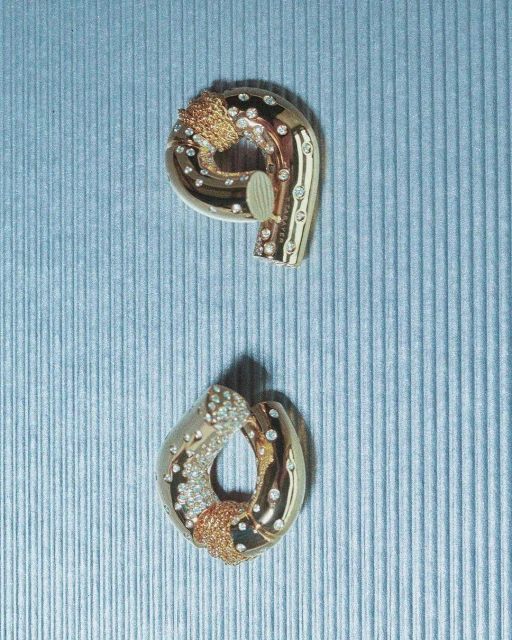Two gold-toned jewellery pieces featuring gem stone accents are presented against a grooved blue background, in an indoor studio-like setting.
