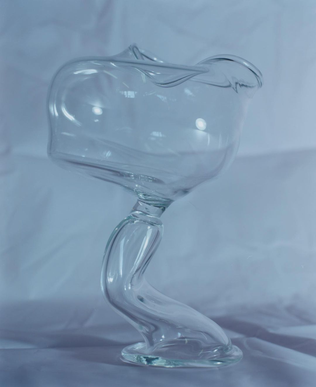 Elegant clear glass vase with a twisted stem on a white surface, showcasing modern design and translucent material in soft lighting.