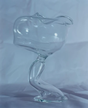 Elegant clear glass vase with a twisted stem on a white surface, showcasing modern design and translucent material in soft lighting.