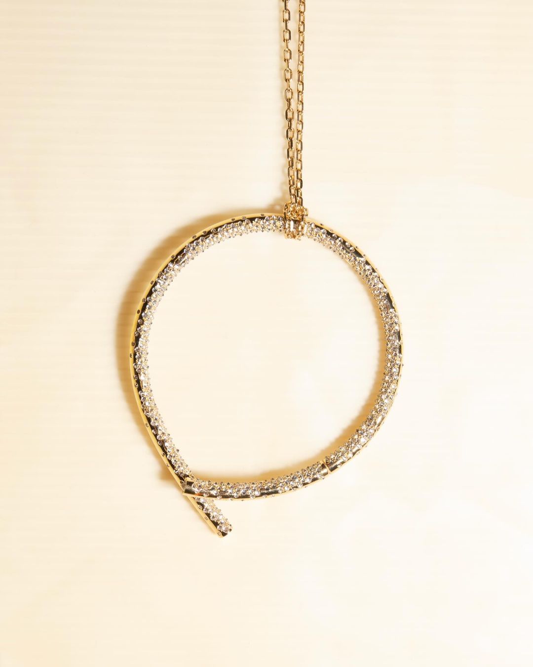 Elevated shot of a circular gold necklace featuring clear gems, gracefully suspended against a soft, neutral backdrop. Minimalist aesthetic.