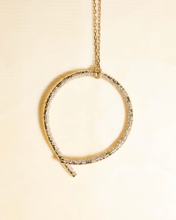 Elevated shot of a circular gold necklace featuring clear gems, gracefully suspended against a soft, neutral backdrop. Minimalist aesthetic.
