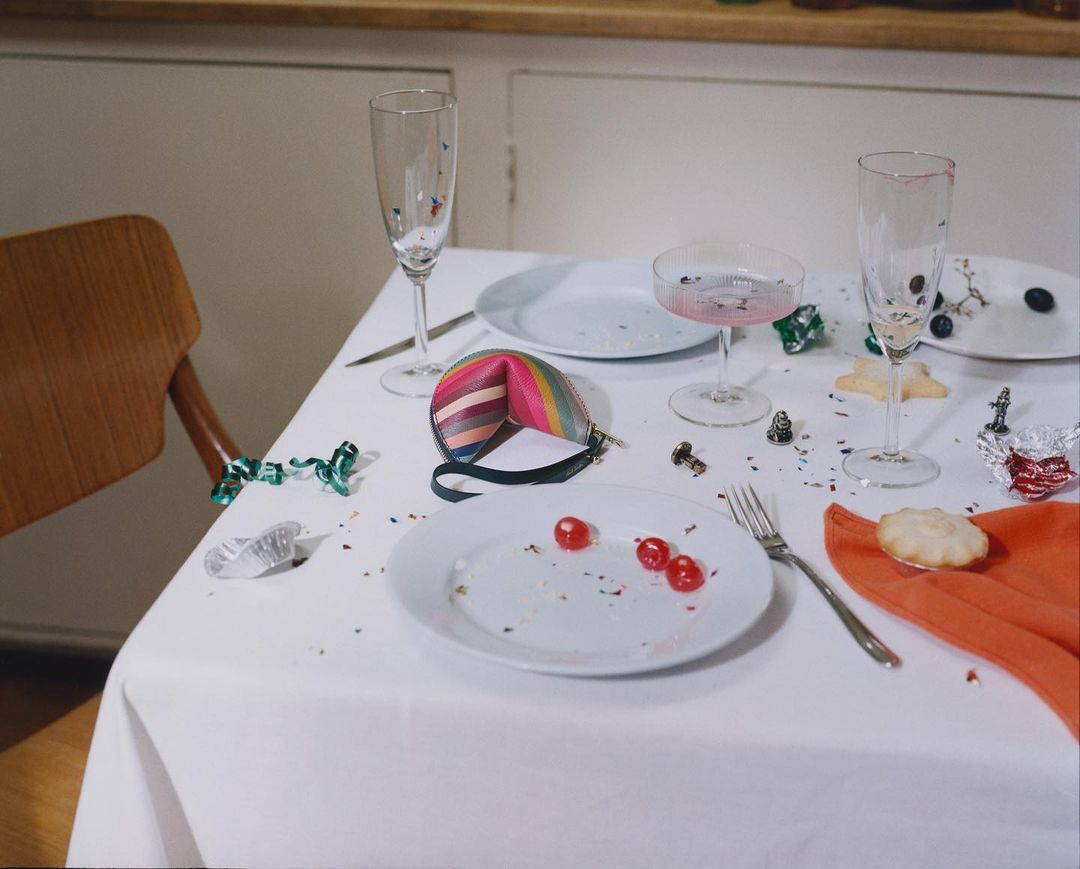 Celebratory table setting with confetti, empty champagne flutes, plates with food remnants, orange napkin, and a striped coin purse.