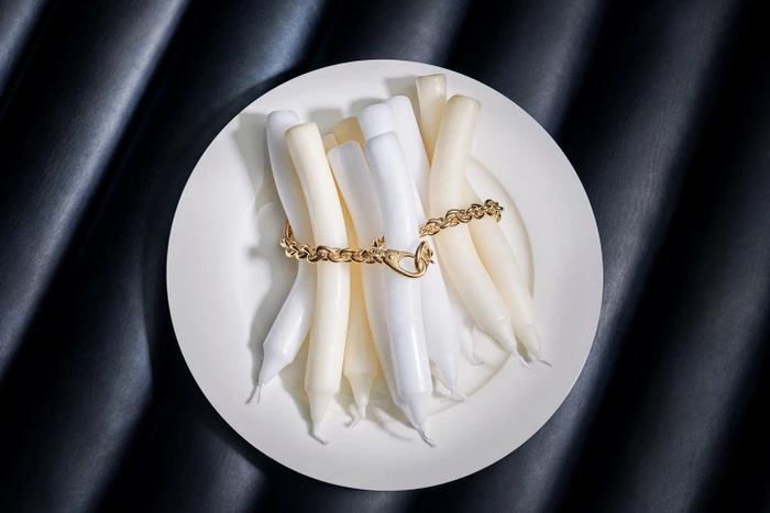 White and cream wax candles bundled together on a white plate bound by a gold chain against dark leather