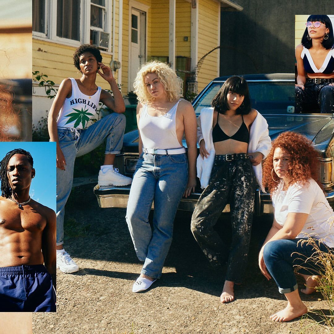 A diverse group of young adult women in casual summer fashion pose outdoors near a weathered yellow house and a vintage car.