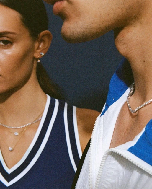 Close-up of a stylish couple with diamond jewelry, one wearing a navy tank top and the other in a white and blue athletic jacket.