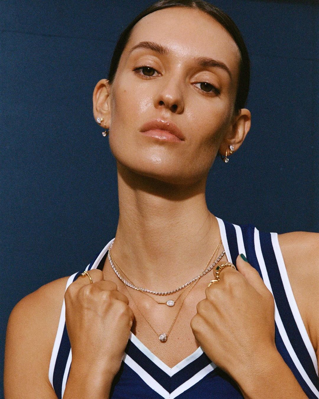 Close-up of an adult woman with fair skin, wearing jewelry and a sporty tank top, against a dark blue background.
