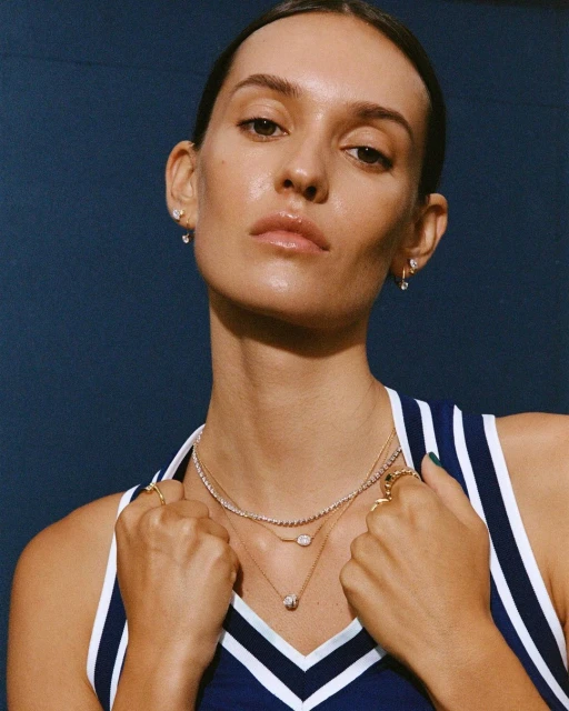 Close-up of an adult woman with fair skin, wearing jewelry and a sporty tank top, against a dark blue background.