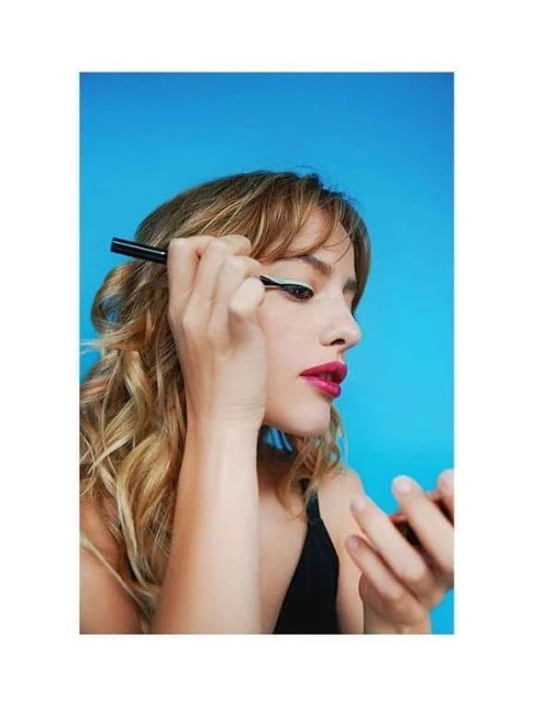 Adult woman applying white eyeliner in a studio setting against a vibrant blue backdrop, showcasing beauty and cosmetic application.