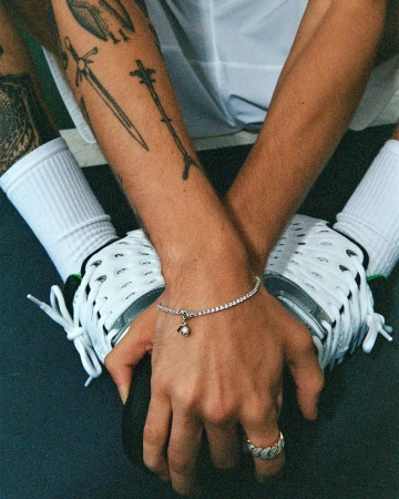 Close-up of a light-skinned adult male's hands wearing a diamond tennis bracelet and ring, holding a black bowling ball.
