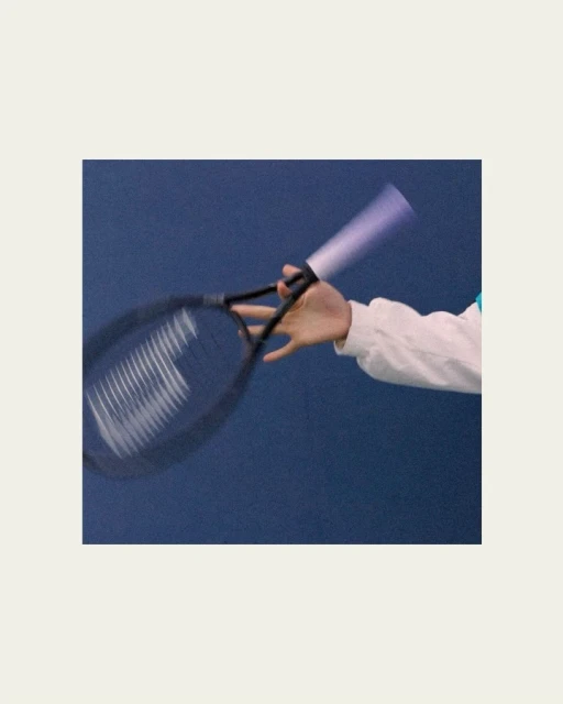 Action shot of a tennis racket in motion held by a person wearing a white sleeve against a dark blue background, capturing a dynamic moment.