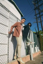 Two models standing near a chain link fence outdoors, shot from a low angle by photographer Cully Wright.