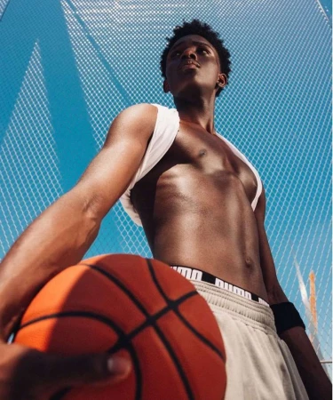 Young Black man holding a basketball outdoors against a chain-link fence by Curtis Jehsta