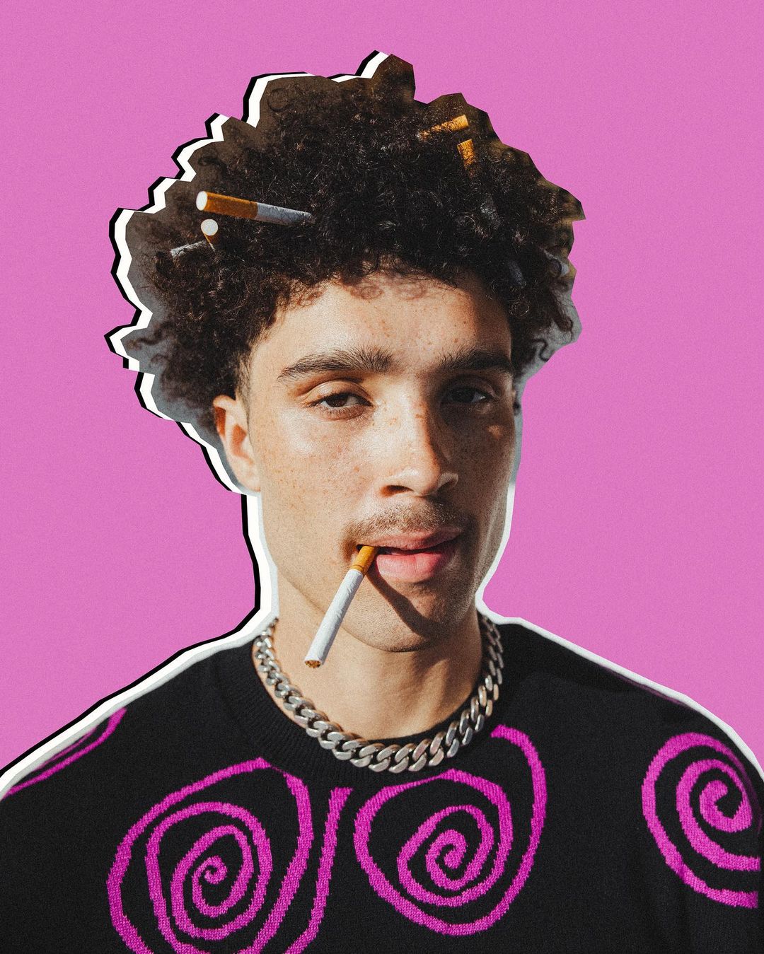 Man with afro wearing sweater with pink design and silver chain smoking cigarette against pink background with white outline. 