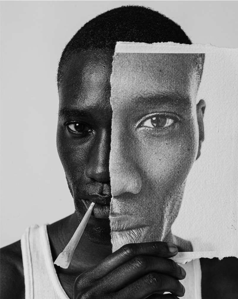 Monochrome portrait of a Black man holding a torn portrait of his own face, creating a layered effect with stark contrasts and textures.
