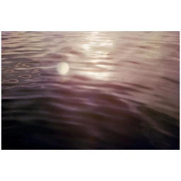Gleaming ripples on water surface with a soft white orb floating, photographed by Cyrille De Vignemont in Paris.